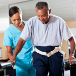 A nurse helping an older man with a gait belt.